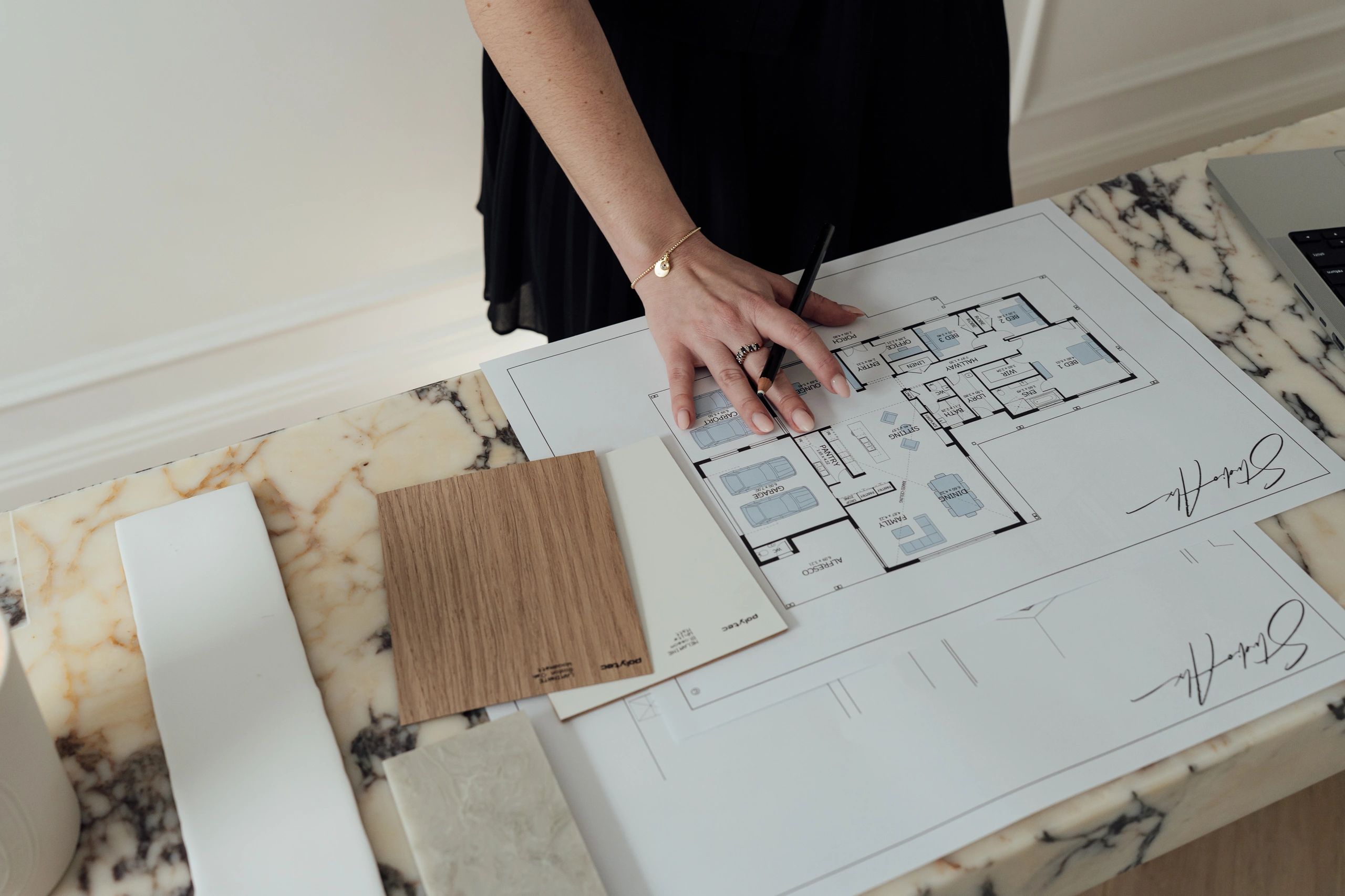 Person reviewing a house floor plan with design samples on a marble table.
