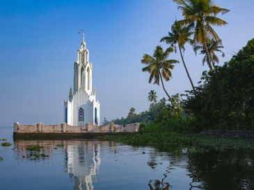 White tower by calm water with palm trees nearby.