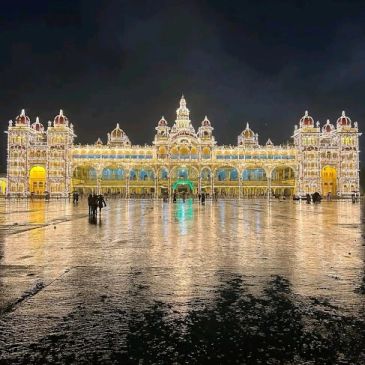 Illuminated Mysore Palace at night with reflections on wet ground.