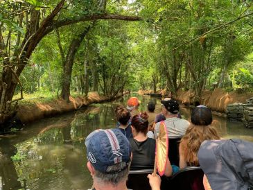 People boat through a lush, tree-lined canal.