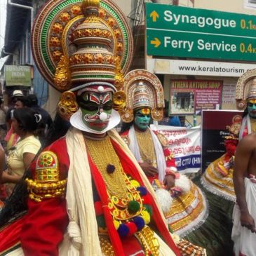 Traditional Kathakali performers in elaborate costumes on a street.