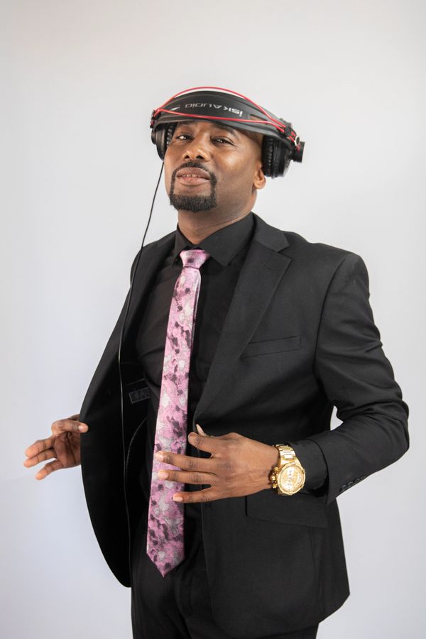 Man in black suit with pink tie and headphones on his head.