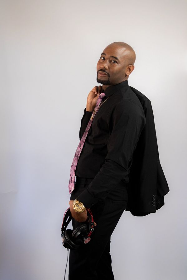 Man in black outfit with pink tie holding headphones and jacket.