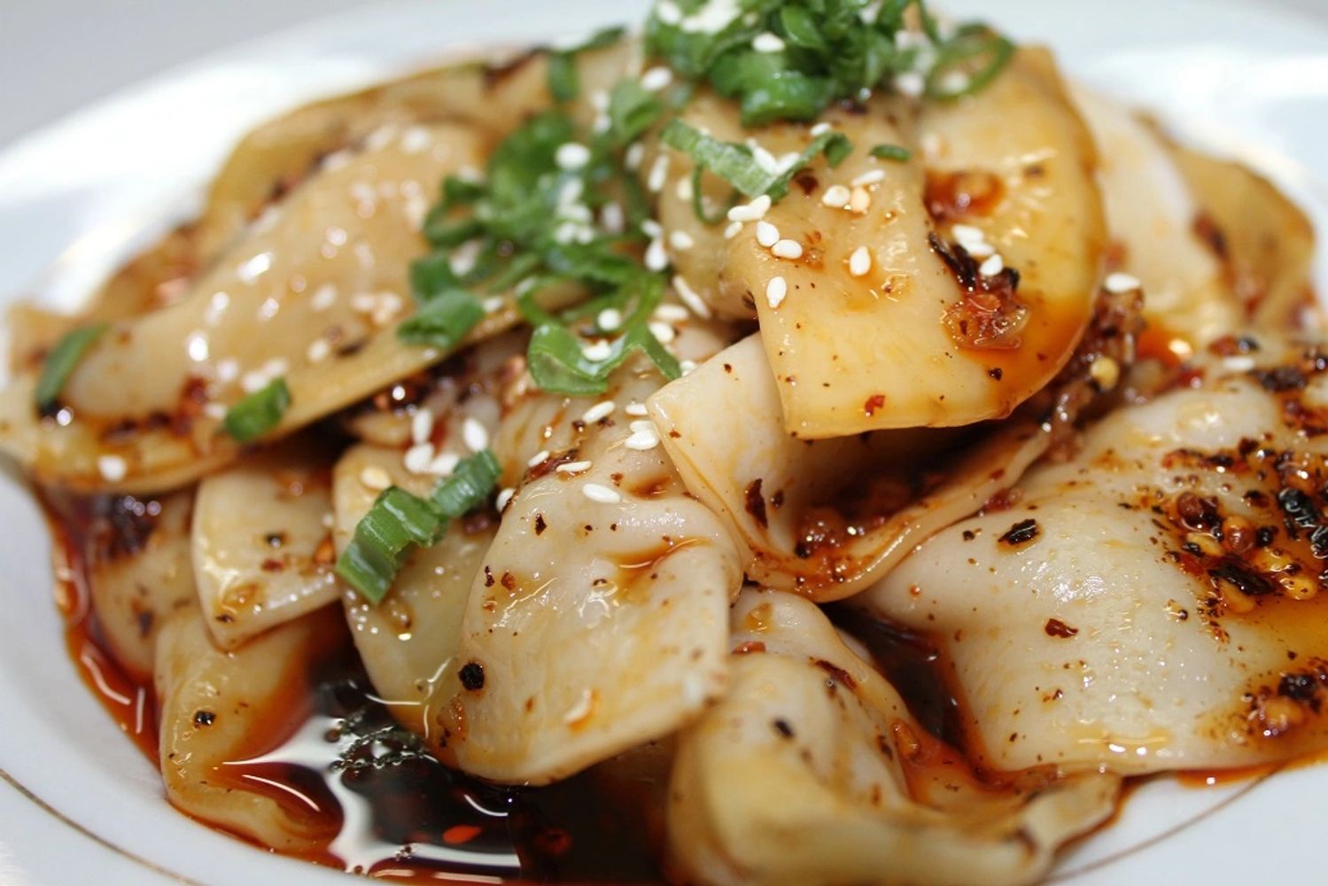 Appetizing dumplings with sauce and chili topped with fresh green onions.