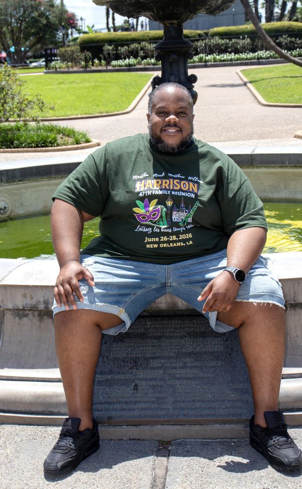 Man sitting by a fountain in a park, smiling.