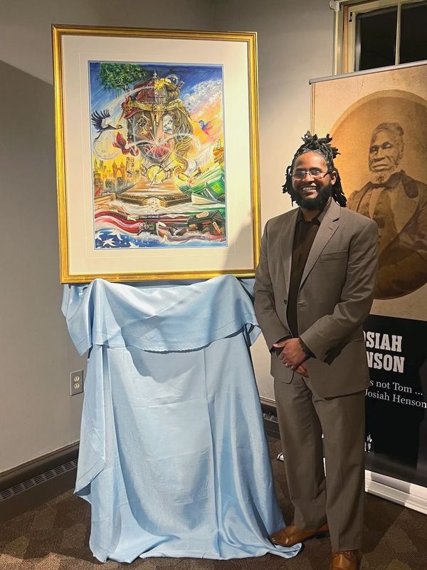 artist in brown suit standing next to gold framed painting with a photo of Josiah Henson.