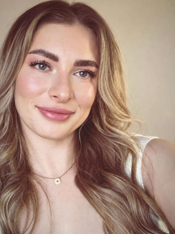 Smiling woman with long wavy hair and a pendant necklace.