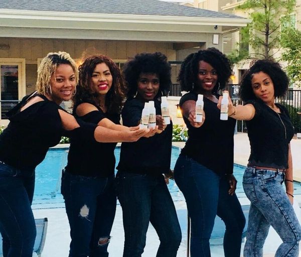 Five women in black tops holding skincare products by a pool, smiling at the camera.