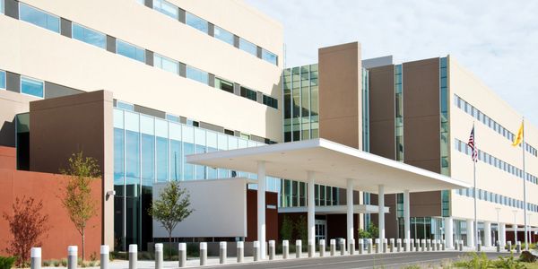 Modern hospital entrance with a covered drop-off area and flagpoles.