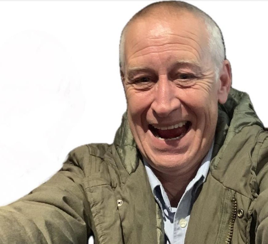 Smiling elderly man wearing a green jacket, taking a selfie.