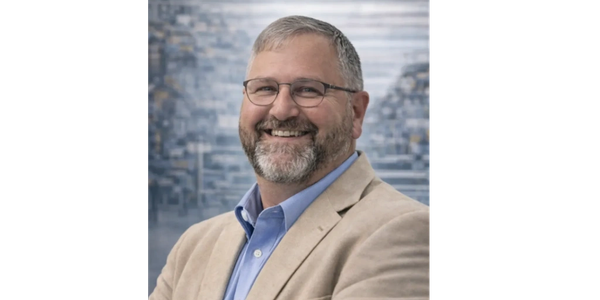 Smiling man with glasses and beard wearing a beige blazer.