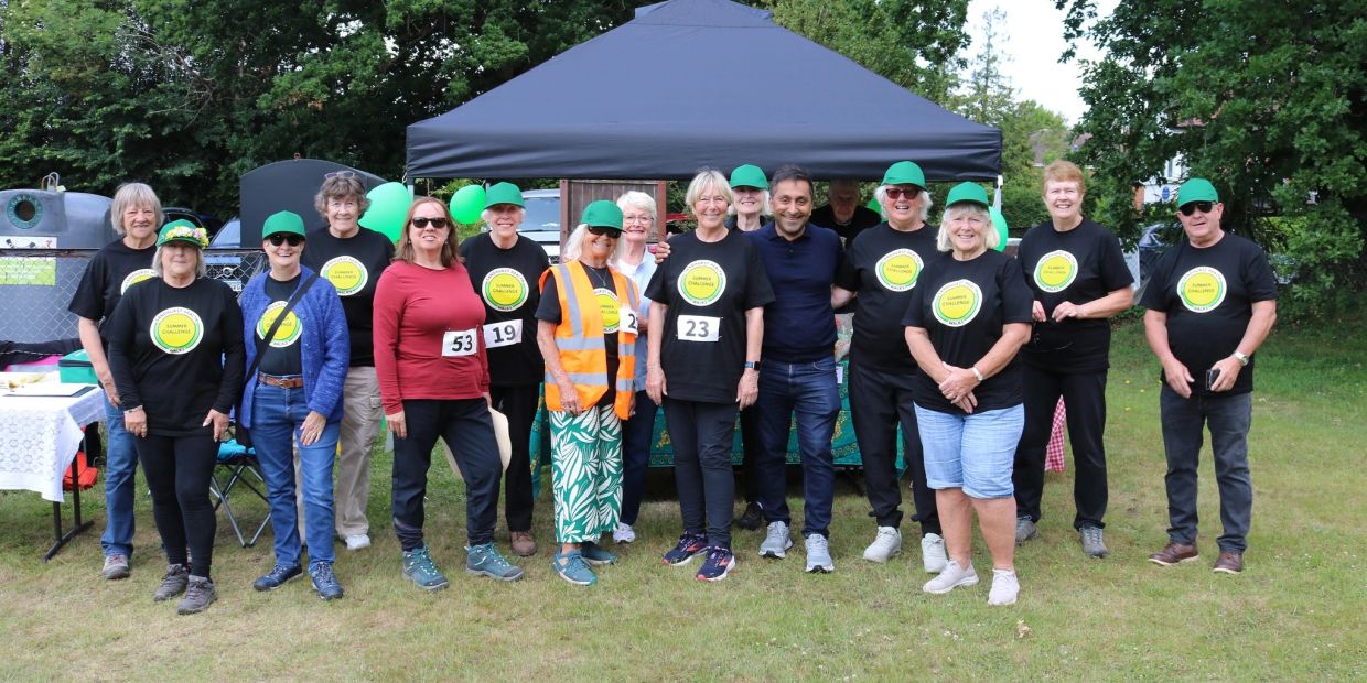 Group of people in matching event shirts and green caps posing outdoors under a canopy.