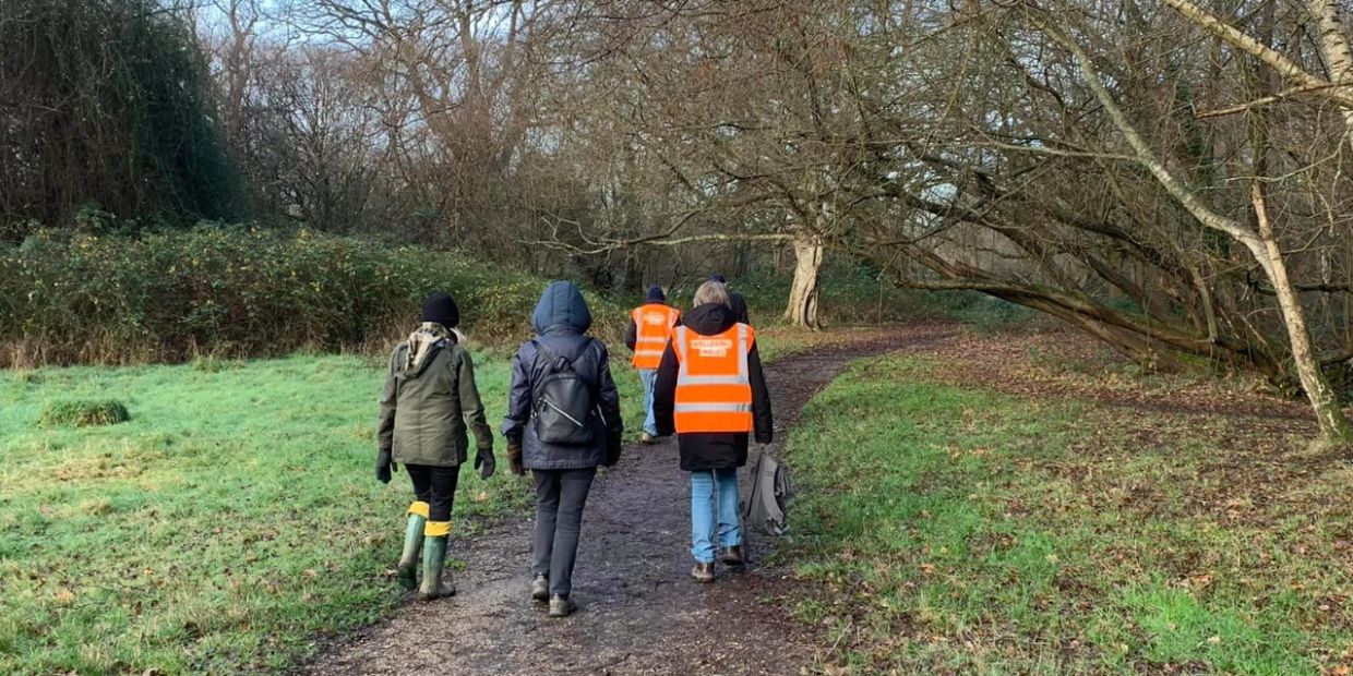 People walking on a forest path, some wearing orange safety vests.