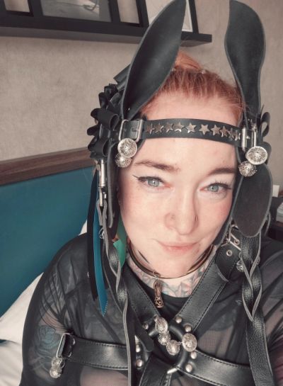 Person wearing leather and metal harness with bunny ears headpiece.