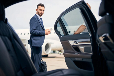 Chauffeur opens door for executive client arriving at private jet, showcasing Platinum Transportation Group’s elite airport car service.