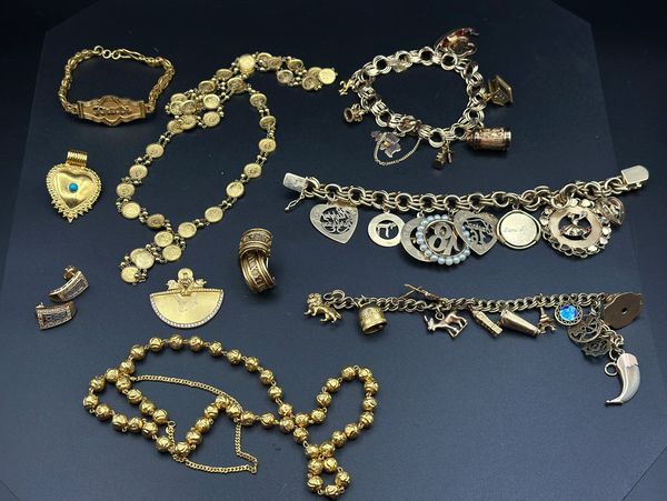 Collection of vintage gold and silver charm bracelets and jewelry on black background.