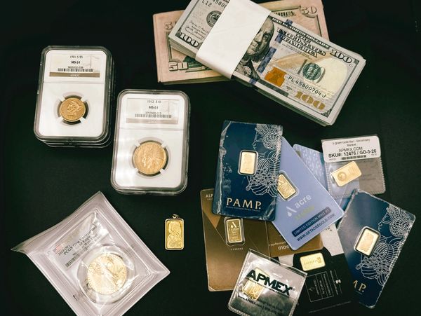 Collection of gold coins, gold bars, and US dollar bills on a black surface.