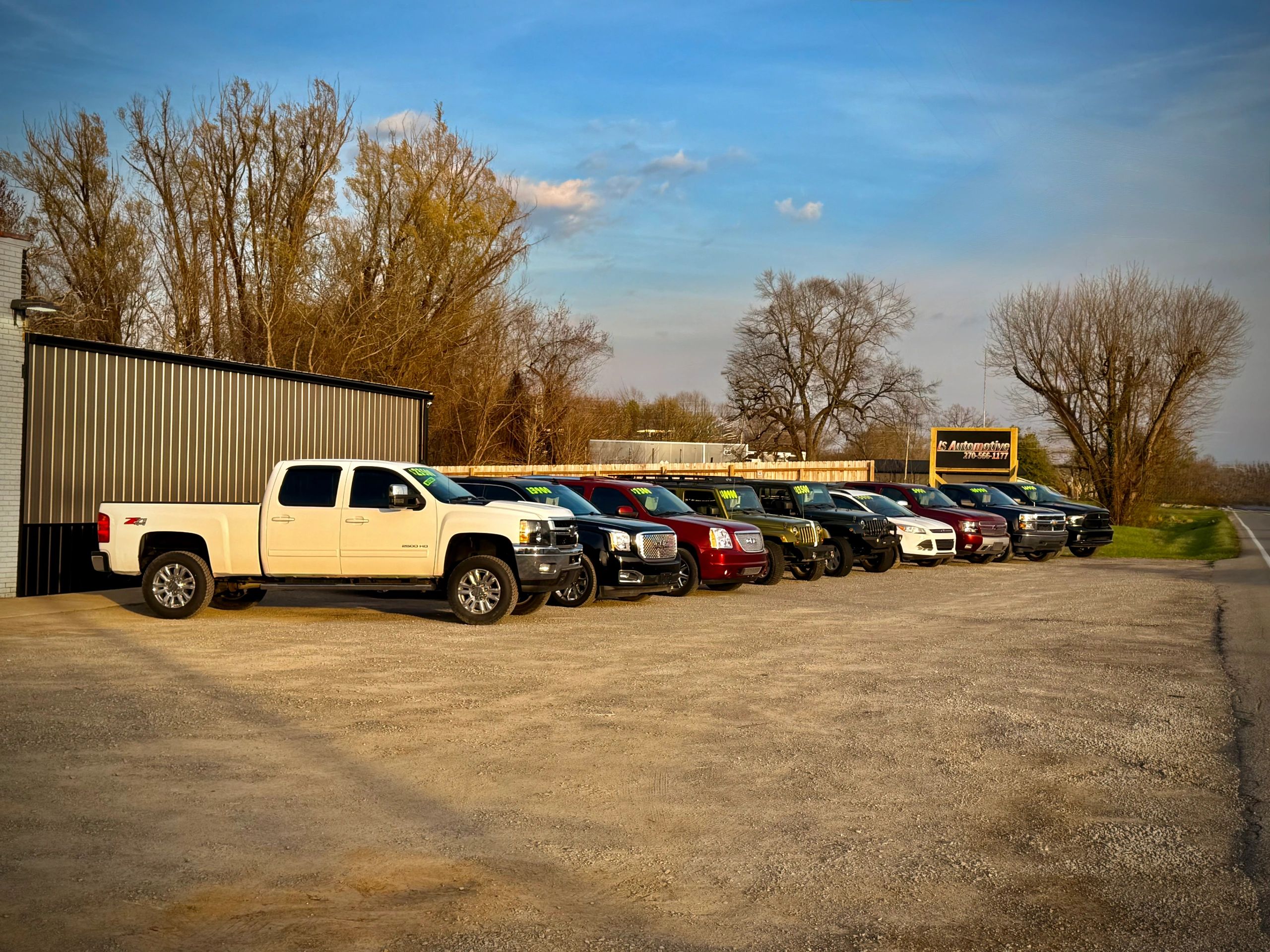 A lineup of various cars and trucks parked outside an automotive dealership.