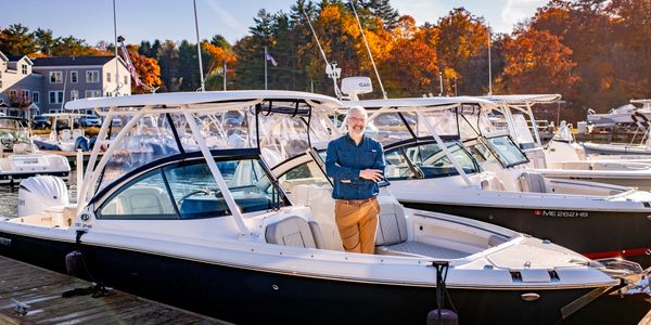 Man standing on a boat docked at a marina with autumn trees in the background.