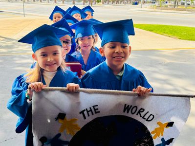 Kids in blue graduation gowns holding a banner.