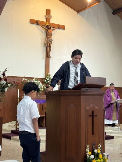Young boy speaking at church podium with crucifix behind.