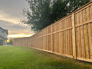 Long wooden fence beside a grassy yard at sunset.