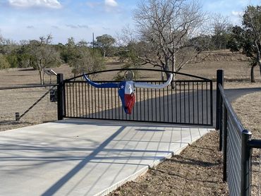 A driveway gate with a Texas-themed longhorn skull on a sunny day.