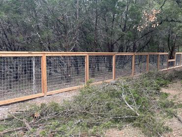 Long wooden fence with wire mesh in a wooded area with fallen branches.