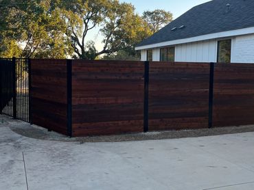 Modern wooden fence with black metal frame around a white house patio area.
