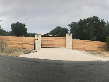 Wooden fence with stone pillars and a gated driveway on a cloudy day.