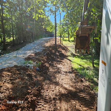 Excavator bucket over a freshly graded dirt and gravel road in a wooded area.