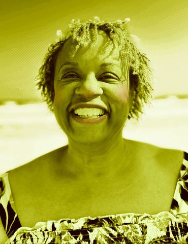 Joyful woman with curly hair smiling brightly outdoors.