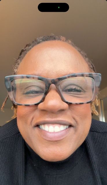 Close-up of a smiling person wearing large tortoiseshell glasses and a black top.