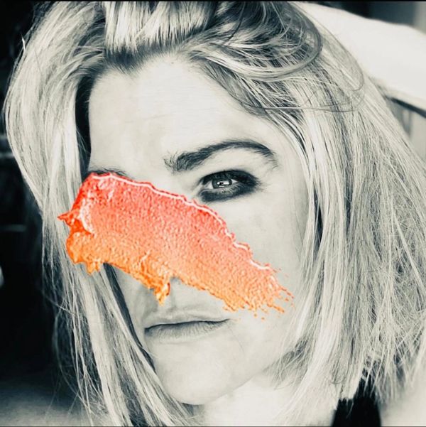 Black and white portrait of a woman with a bold orange paint streak across her face.