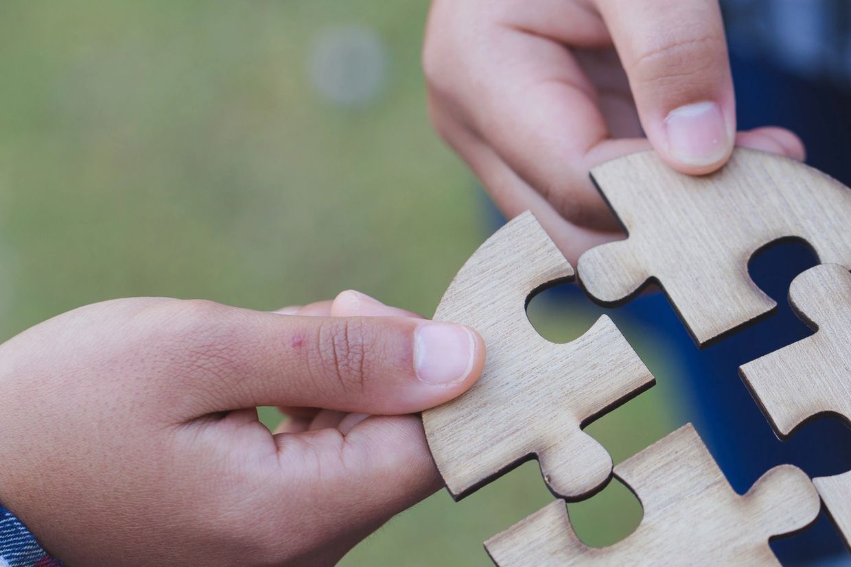 Image of four hands putting four puzzle pieces together.