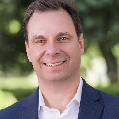 Smiling man in a blue suit jacket outdoors.