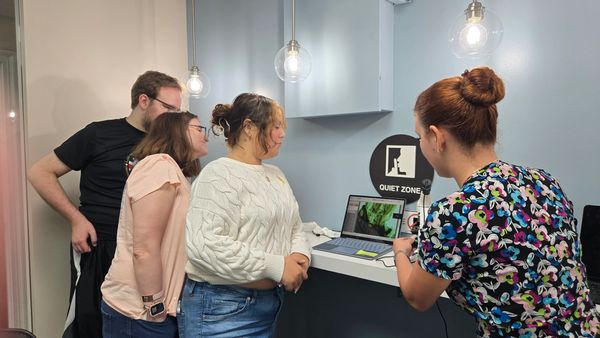 Four people gathered around a laptop in a quiet zone, engaged in a discussion.
