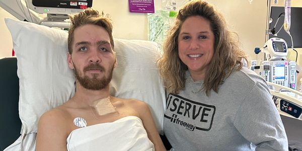A patient with medical adhesive on chest and a woman smiling beside him in a hospital room.