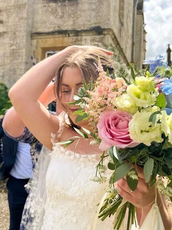 A bride holding her bridal bouquet of pink,  cream and blue flowers