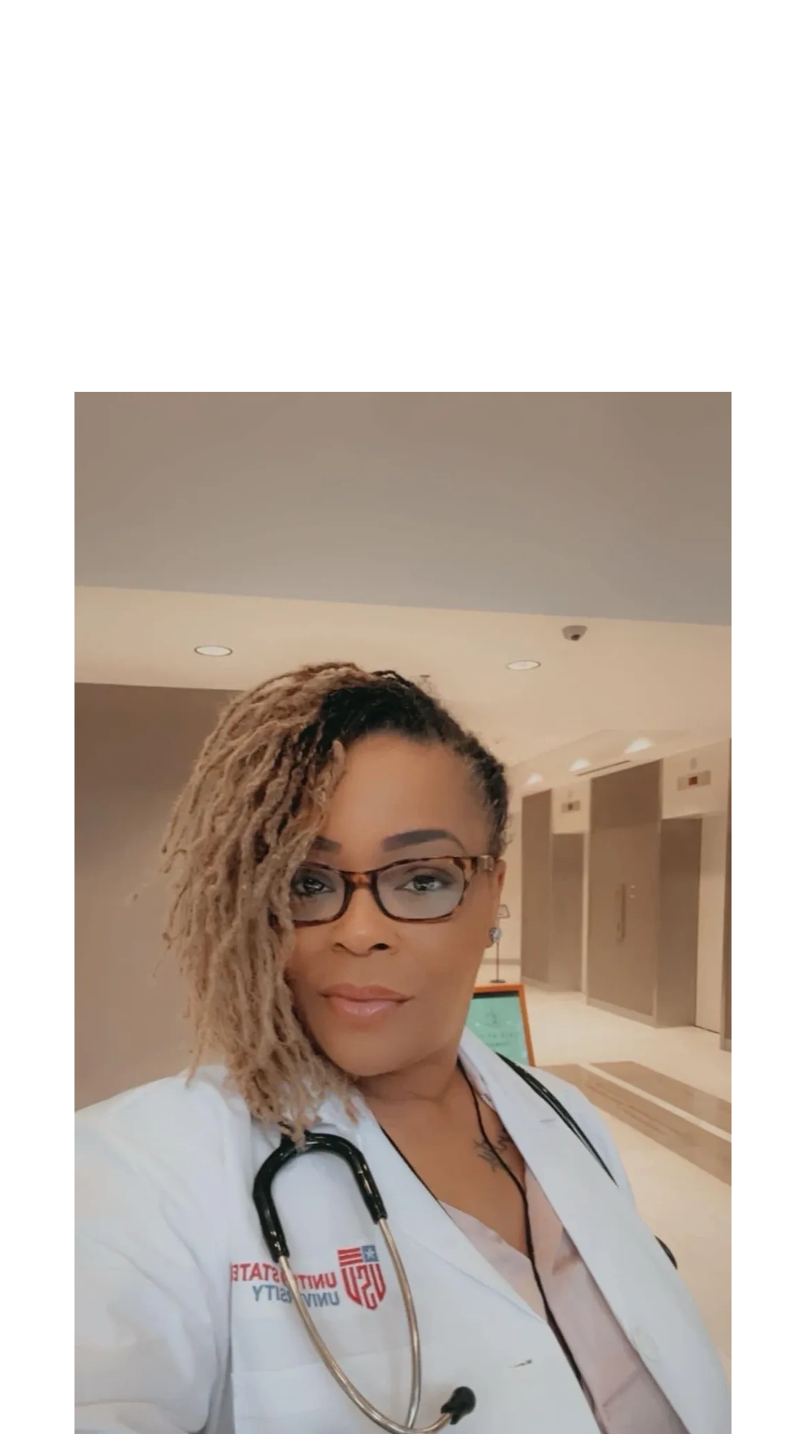 Confident female doctor in white coat with stethoscope in a hospital corridor.