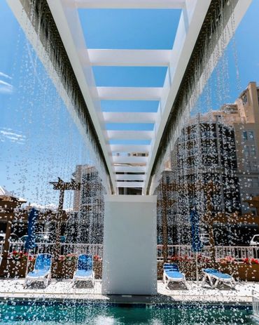 Water cascading from a modern white pergola into a pool under a clear blue sky.