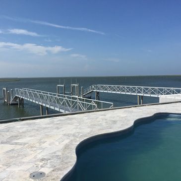 A serene poolside overlooking a calm waterfront with a long dock extending into the water.
