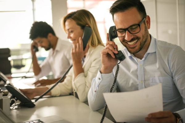Three people working and talking on phones at a desk in a Roofing Company