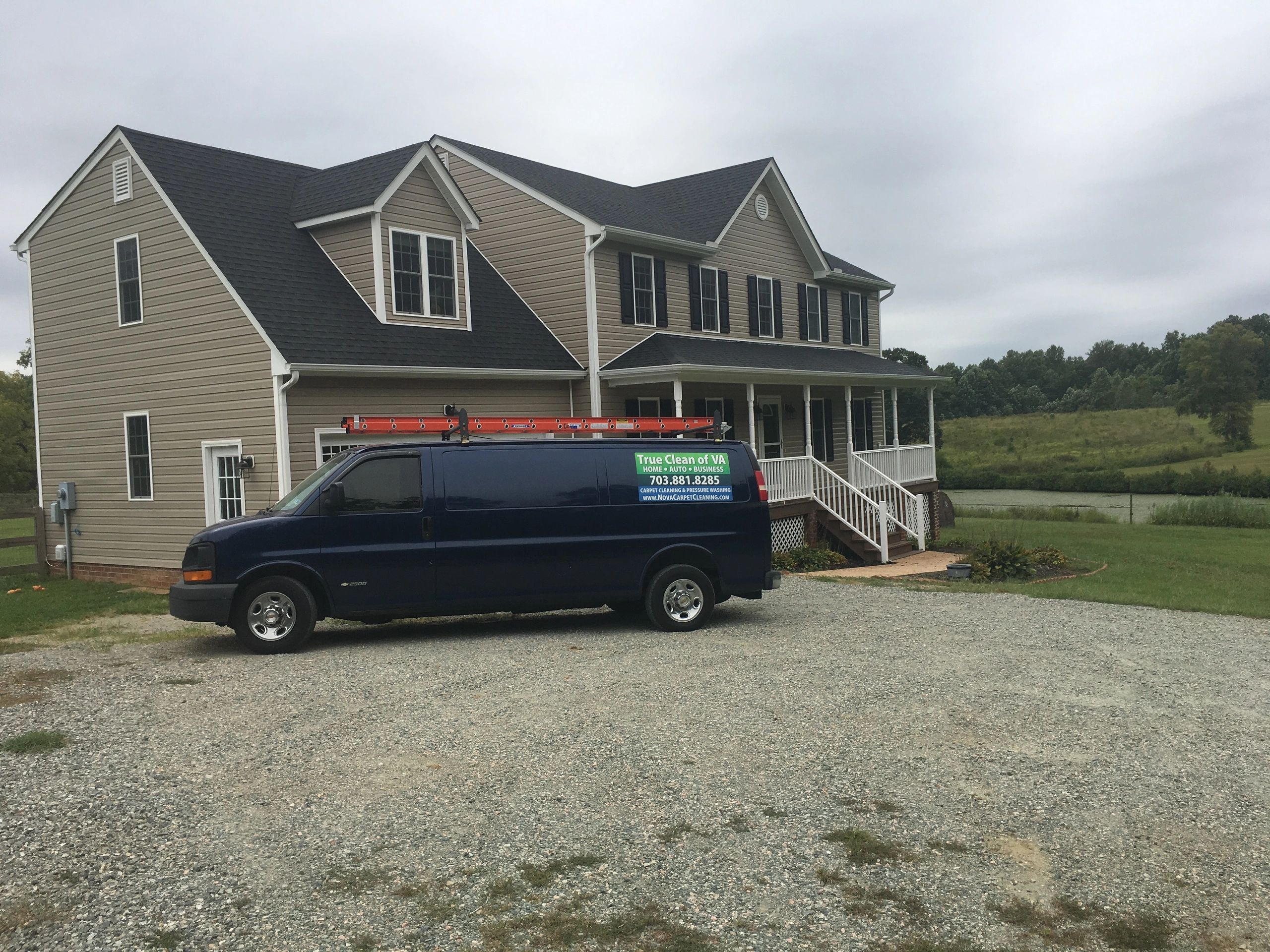 Blue cleaning service van parked in front of a beige two-story house.