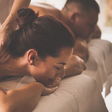 A woman enjoying a relaxing massage with a man in the background.