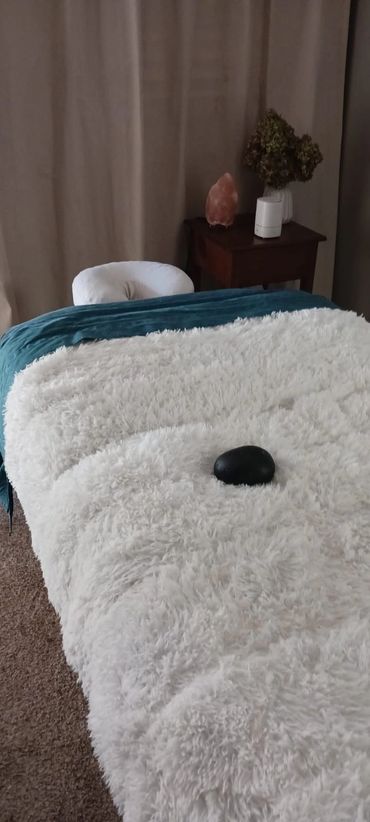 Massage table with a black stone and cozy blankets in a calming room.