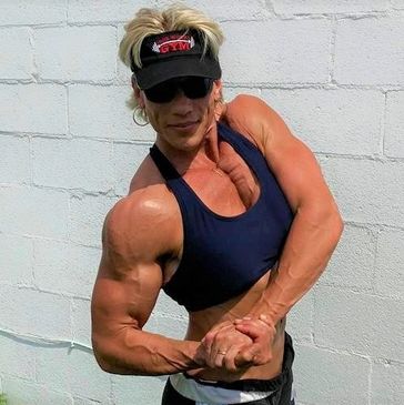Muscular woman flexing her arm muscles against a white wall.