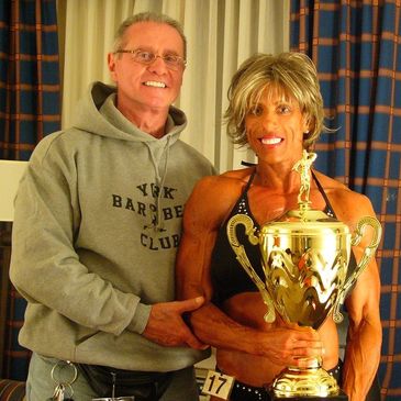 A muscular woman holding a large trophy with a man standing beside her.