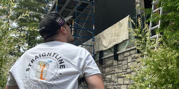 A man wearing a Straightline Painting t-shirt looks up at a building under construction.