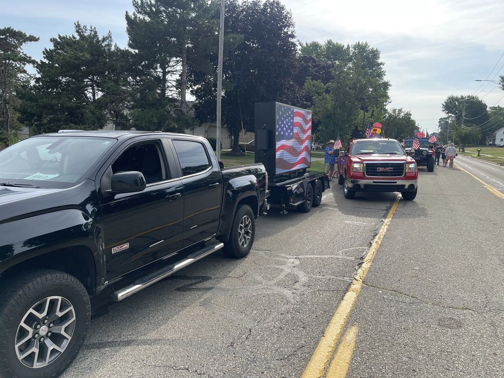 Pickup trucks and a trailer with an American flag display in a parade.
